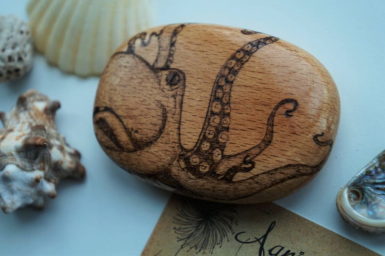 May include: A wooden coaster with a hand-drawn image of an octopus in black ink. The octopus is curled up with its tentacles visible.