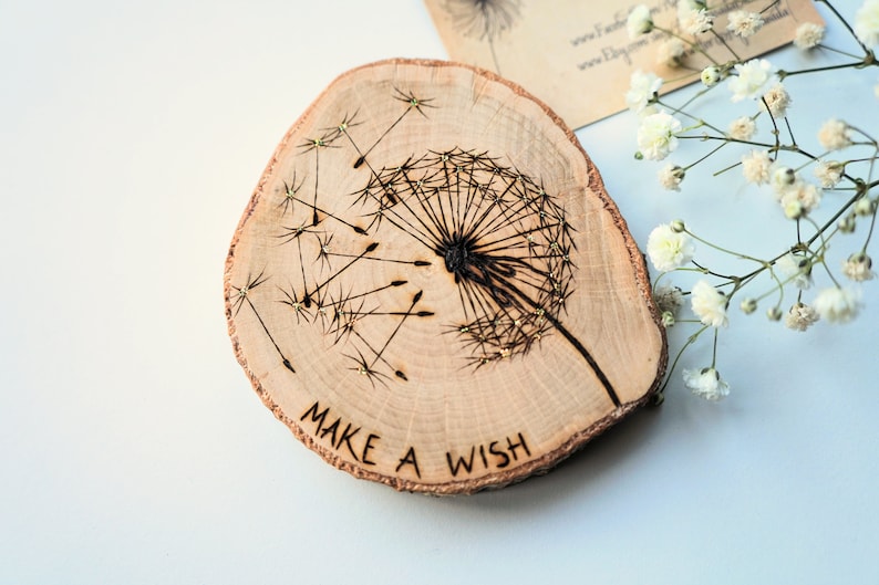 May include: A wooden slice with a burned design of a dandelion with the words "Make a Wish" written below it.
