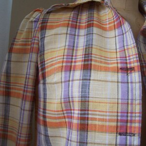 May include: A plaid shirt with a light yellow, orange, purple, and brown plaid pattern. The shirt has a button-up collar and long sleeves.