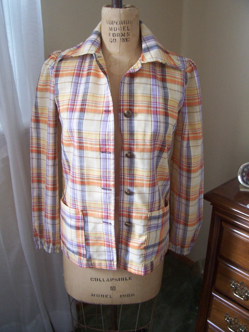 May include: A plaid button-up shirt with long sleeves and a collared neckline. The shirt is in shades of orange, yellow, purple, and white.