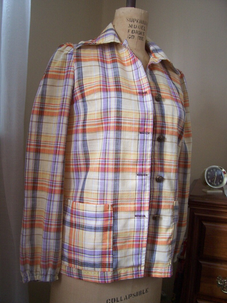 May include: A plaid shirt with long sleeves and a button-up front. The shirt is in shades of orange, yellow, purple, and white.