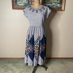 May include: Vintage dress with a grey and white pattern, featuring a navy blue and floral design on the skirt. The dress has a scoop neckline with navy blue trim and cap sleeves. The dress is displayed on a mannequin.