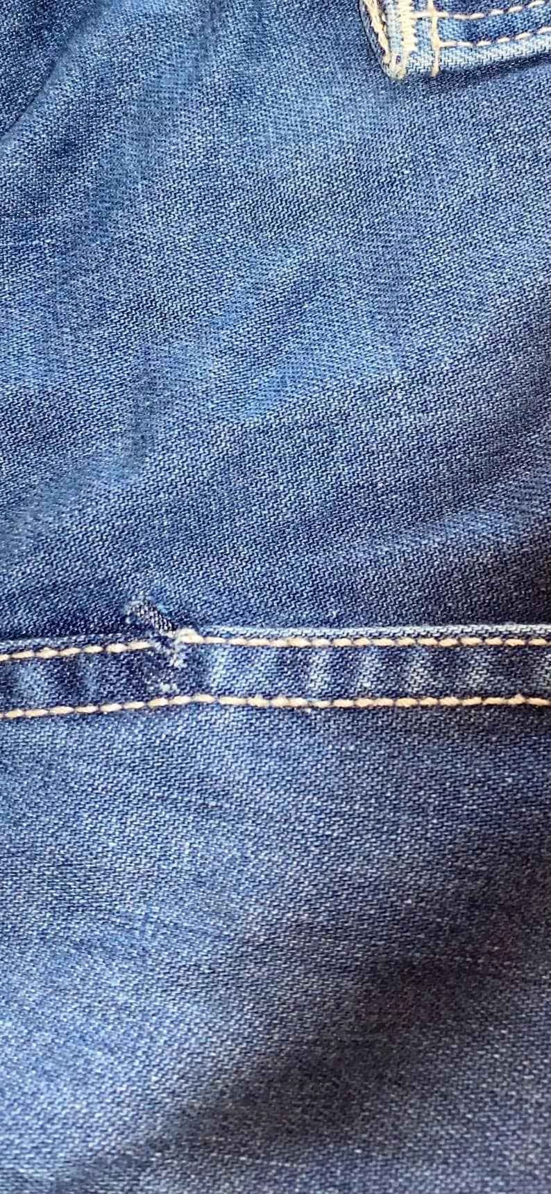 May include: Close-up of blue denim fabric with visible texture and white stitching. The stitching is a prominent design element, adding contrast to the denim. The image highlights the details of the textile.
