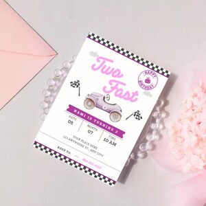 May include: A birthday invitation with a race car theme. The invitation features the text "Two Fast" in pink, along with a vintage car illustration. The invitation includes the date, time, and location details, with a pink envelope and a bouquet of pink flowers in the background.