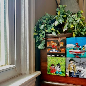 May include: Four square wooden art pieces featuring anime-style illustrations. One depicts a bakery scene, another a boat on water, and two others show characters in a field and with a wolf. The art pieces are displayed on a dark wooden surface.