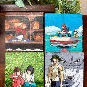 May include: Four square paintings featuring anime characters. One shows a girl in a bakery, another a boy on a boat, a third two children in a field, and the last a woman with a wolf. The paintings are on a wooden surface.