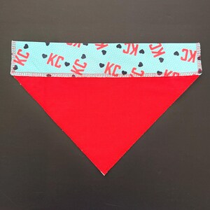 May include: Red and light blue dog bandana. The top section is light blue with the letters "KC" and black hearts. The bottom section is solid red. The bandana is triangular in shape.