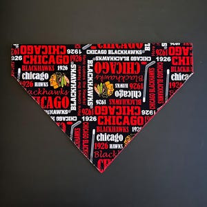 Può includere: Bandana per cani dei Chicago Blackhawks nera e rossa. La bandana presenta il nome della squadra, il logo e l'anno 1926 in un motivo ripetuto. Anche i bastoni da hockey sono inclusi nel design. È presente anche il testo "Here comes the Hawks!"