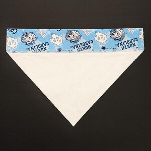 May include: A triangular pet bandana with a light blue top section featuring the words "North Carolina" and the UNC logo in white. The main body of the bandana is white.
