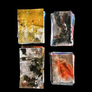 May include: Four stacks of rectangular paper sheets featuring abstract mixed media designs. The top-left stack is yellow and white, the top-right is black and grey, the bottom-left is grey with dark accents, and the bottom-right is grey with orange.