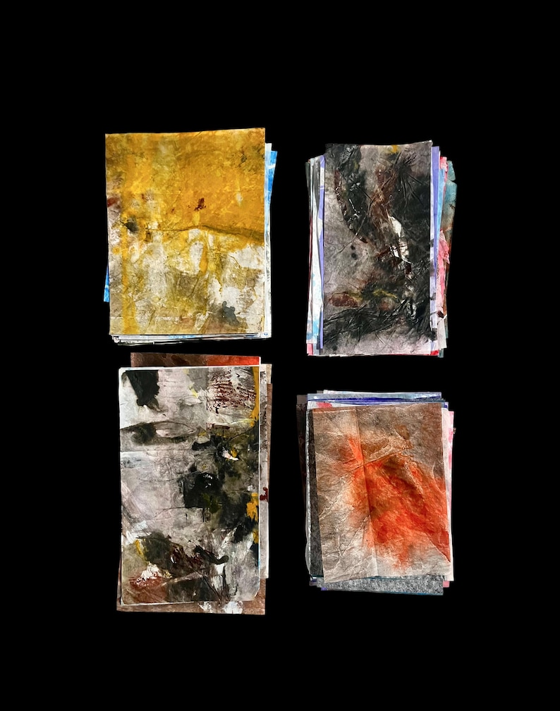 May include: Four stacks of rectangular paper sheets featuring abstract mixed media designs. The top-left stack is yellow and white, the top-right is black and grey, the bottom-left is grey with dark accents, and the bottom-right is grey with orange.