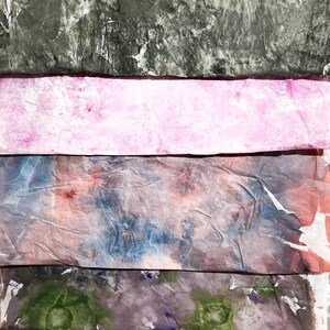May include: Four horizontal strips of textured, crinkled paper arranged in a stack. The top strip is charcoal gray, the second is light pink, the third features a mottled blend of blue and peach, and the bottom strip displays green and purple tones.