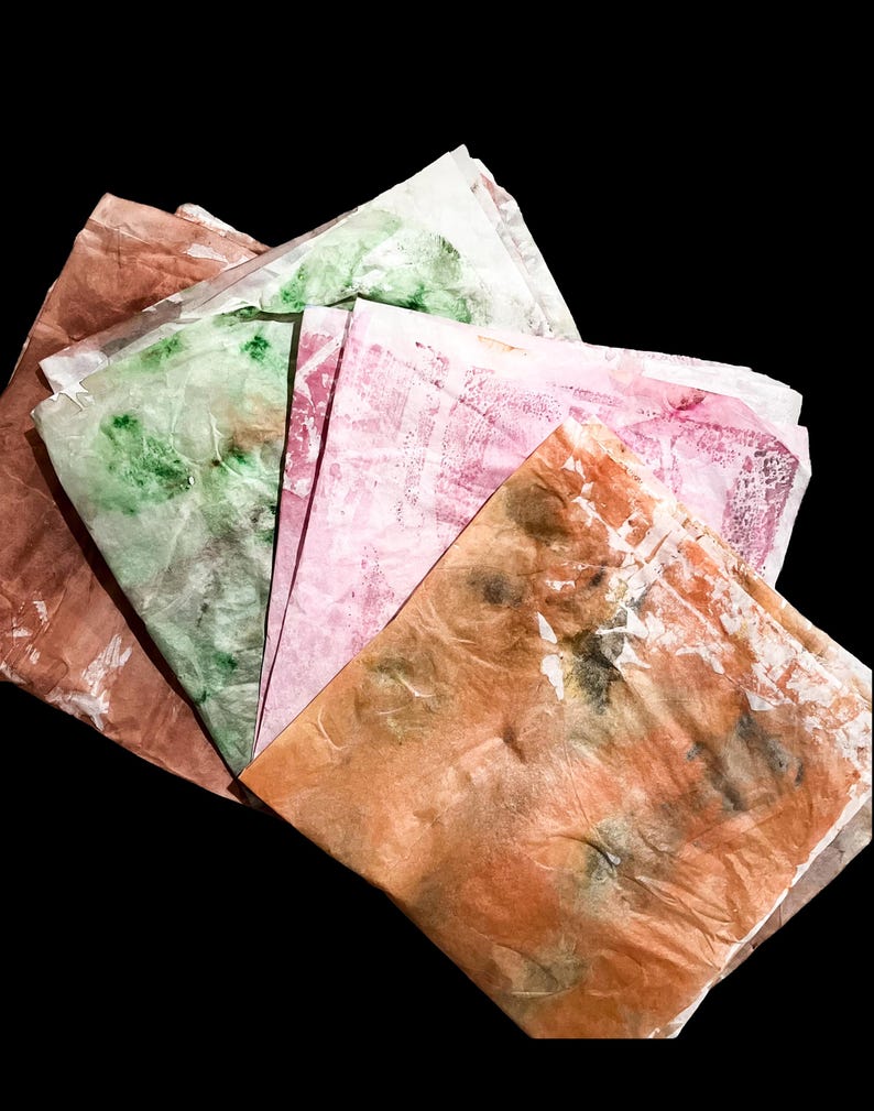 May include: A stack of folded, translucent sheets of paper featuring a marbled, tie-dye effect in various colors including shades of orange, pink, and green. The paper has a crinkled, textured appearance with overlapping layers and irregular patterns.