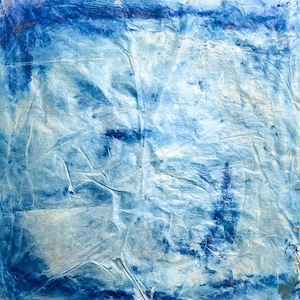 May include: A square sheet of textured paper featuring a gradient of blue and white tones. The surface is heavily creased and wrinkled, creating a complex pattern of light and shadow. Deep indigo pigment is concentrated along the edges.