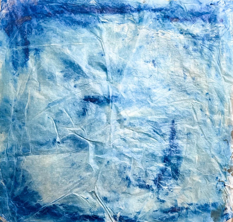 May include: A square sheet of textured paper featuring a gradient of blue and white tones. The surface is heavily creased and wrinkled, creating a complex pattern of light and shadow. Deep indigo pigment is concentrated along the edges.