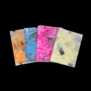 May include: Four rectangular sheets of thin, translucent paper arranged in a fan shape. The sheets feature abstract, mottled patterns in vibrant colors including orange, blue, hot pink, and pale yellow, all accented with dark gray or black ink spots.