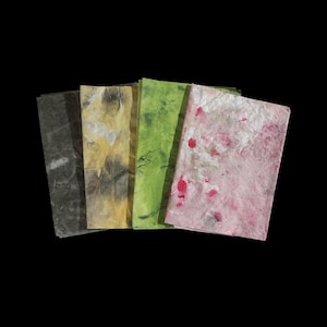 May include: A set of four rectangular sheets of textured paper arranged in a fan shape. The sheets feature marbled patterns in shades of dark gray, muted yellow, vibrant lime green, and a light pink with scattered deep red and white accents.