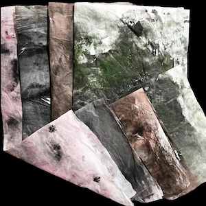 May include: A collection of rectangular sheets of textured paper featuring organic, mottled patterns in shades of pale pink, charcoal gray, earthy brown, and deep forest green, with visible creases and subtle dark speckles across the surfaces.