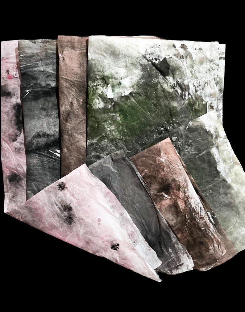 May include: A collection of rectangular sheets of textured paper featuring organic, mottled patterns in shades of pale pink, charcoal gray, earthy brown, and deep forest green, with visible creases and subtle dark speckles across the surfaces.