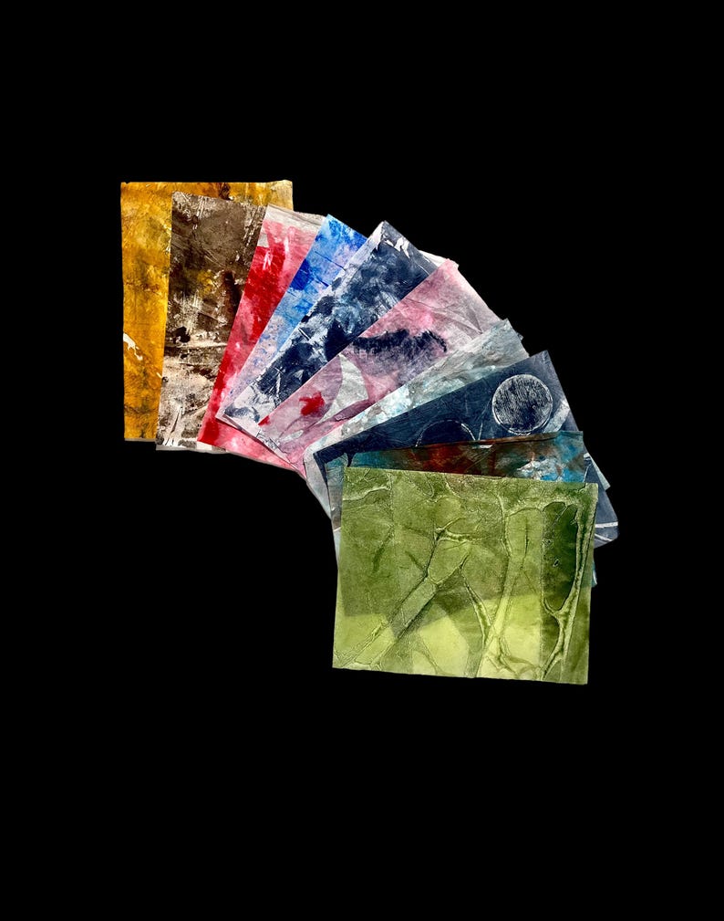 May include: A collection of rectangular paper sheets arranged in a fan shape. Each sheet features a unique abstract pattern with varied textures and colors, including yellow, brown, red, blue, pink, and green, with some showing circular motifs.