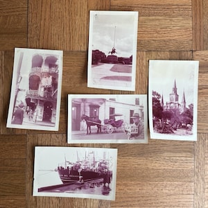 May include: A collection of vintage sepia-toned postcards. The postcards depict various scenes, including architecture, a horse-drawn carriage, a ship, and a statue. The images are printed on aged paper, suggesting they are antique.