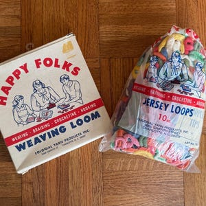 May include: Two vintage craft items: a box labeled "Happy Folks Weaving Loom" and a bag of "Jersey Loops" yarn. The box is beige with red and blue text and illustrations. The bag contains colorful fabric loops, weighing 10 oz.