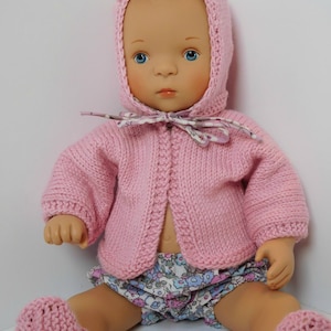 以下が含まれることがあります： フード付きのカーディガンとブーティが付いたピンクのニット製ベビー人形の衣装。人形は花柄のオムツを着用しています。