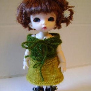 May include: A doll with brown hair wearing a green and yellow knitted dress and black shoes.