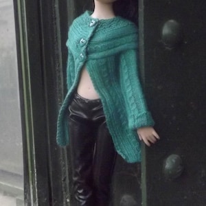 May include: A doll wearing a teal knitted beret and a matching teal cable-knit cardigan with three buttons, paired with black trousers and black high-heeled boots. The text Cécylia Créations is visible at the top of the image.