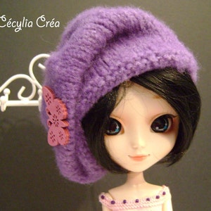 May include: A purple knitted beret with a pink butterfly embellishment on a doll with black hair and large blue eyes.