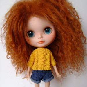 May include: A doll with long, curly, red hair wearing a yellow knitted sweater and blue denim shorts.