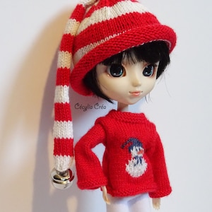 May include: A doll wearing a red and white striped knit hat with a bell on the end, a red sweater with a snowman design, and white pants.