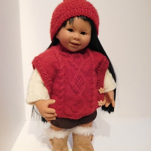 以下が含まれることがあります： 白いポンポンが付いた赤いニット帽、ケーブル編みの赤いニットベスト、白いファーのトリムが付いた茶色のブーツ。人形は衣装を着ていて、長い黒髪をしています。