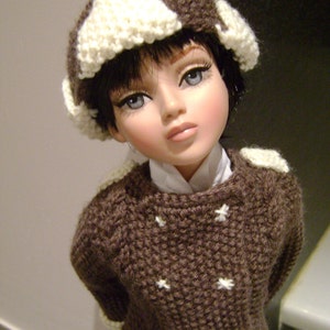 Puede incluir: Un suéter de punto marrón con detalles de estrellas blancas y un gorro de punto blanco con detalles marrones. El suéter tiene un cuello de tortuga.