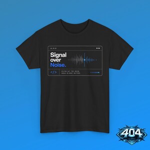 May include: A black short-sleeve t-shirt featuring a white rectangular graphic box containing a sound wave visualization. The text reads Signal over Noise. along with the code snippet symbol, v1.0.0, and the phrase Filter out the noise. Focus on what matters.