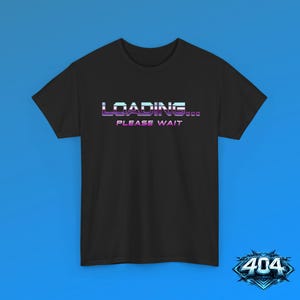 May include: A black short-sleeved t-shirt featuring the text LOADING... PLEASE WAIT in a stylized, gradient font with shades of blue, purple, and white. The design is centered on the chest, and the shirt has a standard crew neckline and short sleeves.