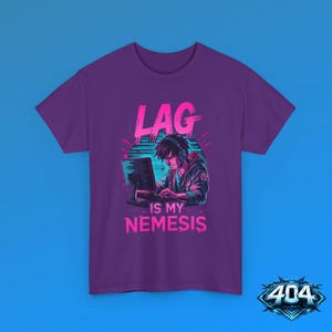 May include: A purple short-sleeve t-shirt featuring a graphic of a person wearing headphones at a computer. The text above reads LAG and the text below reads IS MY NEMESIS in bright pink. The design uses neon blue and pink color accents.