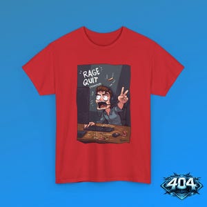 May include: A red t-shirt featuring a graphic illustration of a person wearing a headset, sitting at a computer desk, and making a peace sign gesture. The text RAGE QUIT CHAMPION is printed above the person, who has an open-mouthed expression.