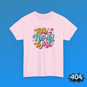 May include: A light pink short-sleeve t-shirt featuring a colorful graphic print that reads Talk Nerdy To Me in stylized lettering. The design includes a pair of pink glasses, a small heart speech bubble, a pencil, and tiny star accents.