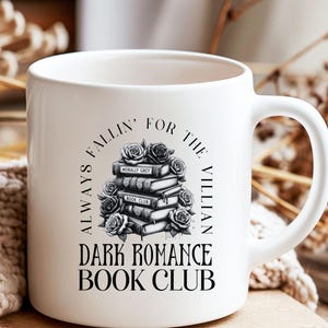 May include: White ceramic mug with the text "ALWAYS FALLIN' FOR THE VILLIAN DARK ROMANCE BOOK CLUB" in black. The design includes a stack of books and roses. The mug has a curved handle.