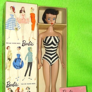 May include: Vintage Barbie doll in original box. The doll wears a black and white striped swimsuit. The box features illustrations of Barbie in various outfits. A pink booklet and sunglasses are also included.