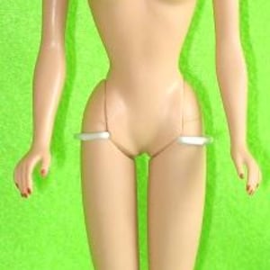 May include: A vintage doll with a slender figure, dark hair styled in a ponytail, and blue eyes. The doll has a fair complexion, red painted fingernails, and is standing on a white base against a green backdrop. The doll is a classic toy.