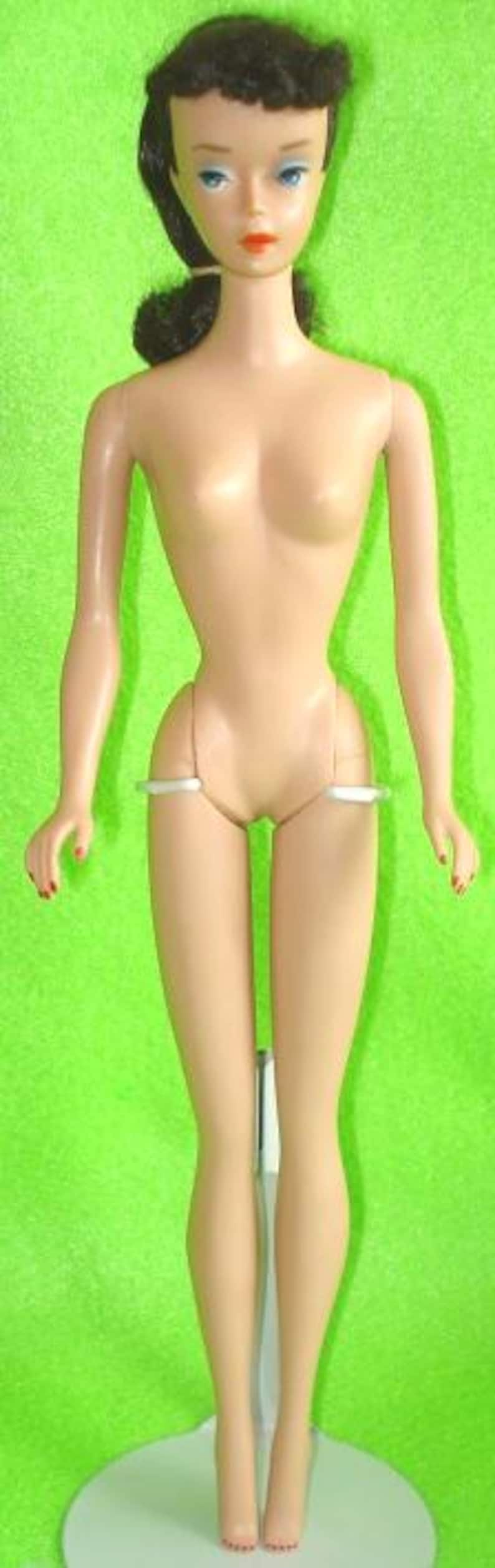 May include: A vintage doll with a slender figure, dark hair styled in a ponytail, and blue eyes. The doll has a fair complexion, red painted fingernails, and is standing on a white base against a green backdrop. The doll is a classic toy.