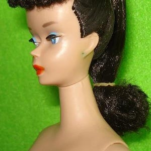 May include: A vintage doll with a fair complexion, blue eye shadow, and bright red lipstick. The doll has black hair styled in a high ponytail and a curled fringe. The doll is a classic toy.