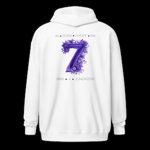 Op de afbeelding: Witte hoodie met een paars bloemmotief met het nummer 7. Het ontwerp bevat de namen JIN, SUGA, J-HOPE, RM, JIMIN, V en JUNGKOOK. De hoodie heeft een capuchon en lange mouwen.