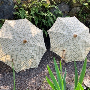 以下が含まれることがあります： 木製のハンドルが付いた白と緑の模様の傘が2つ。傘は閉じており、砂利の地面に置かれています