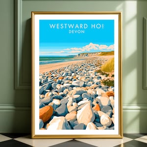 May include: A framed vertical art print featuring a coastal landscape of Westward Ho! Devon. The illustration depicts a pebble beach in the foreground, a sandy shoreline, blue ocean water, and a bright sky. The text reads WESTWARD HO! DEVON.