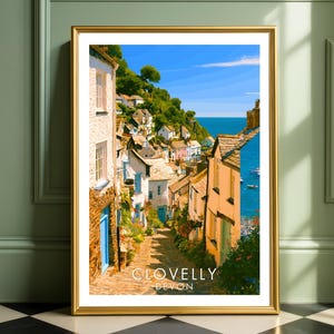 May include: A framed art print featuring a colourful illustration of the coastal village of Clovelly in Devon, England. The scene depicts a steep, cobblestone street lined with white and yellow houses, lush greenery, and a view of the blue ocean.