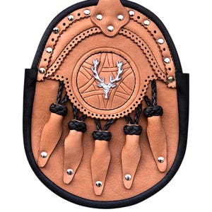 May include: A tan leather sporran with a black border and decorative silver rivets. The sporran features a central embossed design with a silver stag emblem and five tan leather tassels with silver studs.