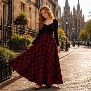 May include: A long-sleeved black top with a sweetheart neckline paired with a floor-length, high-waisted skirt featuring a red and black plaid pattern. The skirt has a full, flared silhouette that reaches the ground, creating a classic look.